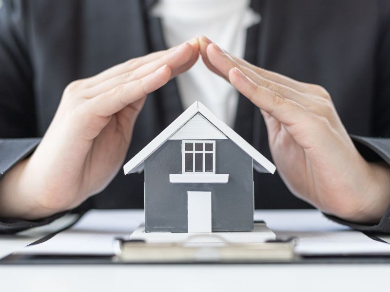 uomo mette due mani sopra un modellino di casa a significare l'assicurazione sulla casa