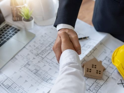 stretta di mano, sullo sfondo planimetria e casa a indicare l'investire nel mattone