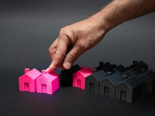 mano spinge due modellini di case rosa accanto a delle case nere